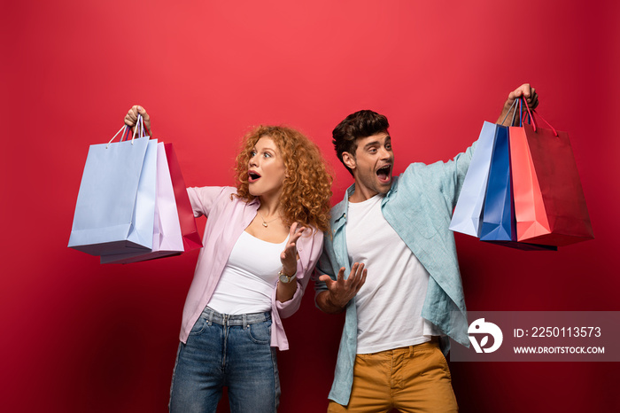 shocked couple looking at shopping bags, isolated on red