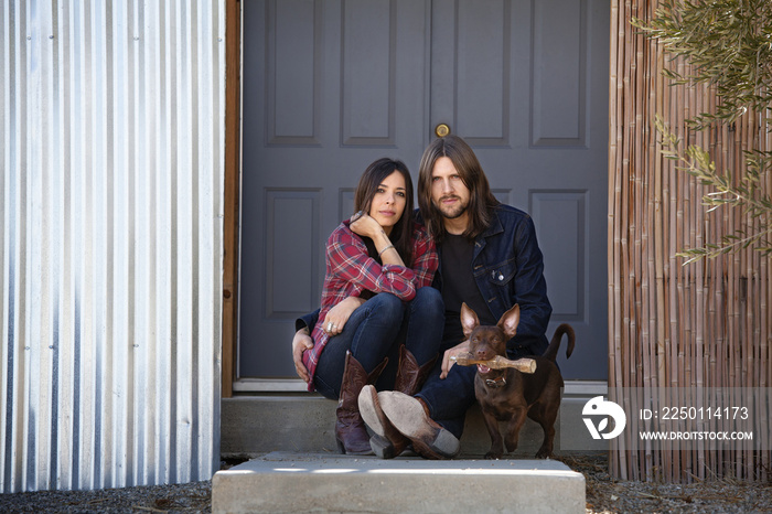 Portrait of couple sitting with dog against door at backyard