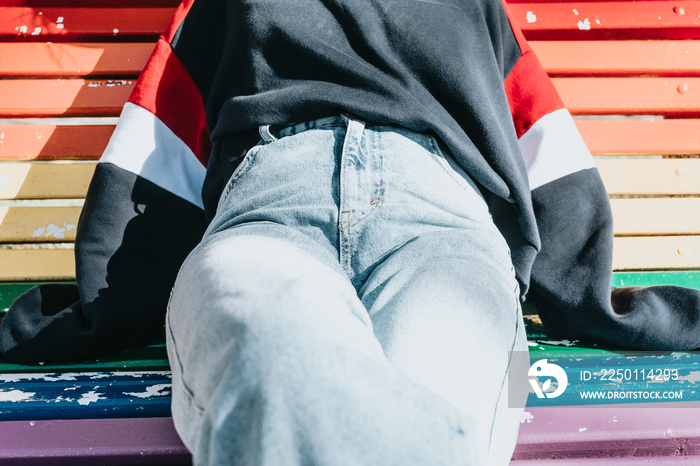 Close up of a woman wearing mom jeans over a rainbow lgbt bench at the park