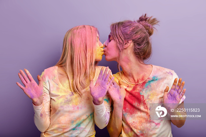 Young best friend females kiss affectionately, have fun together, smeared with colored powder, celeb