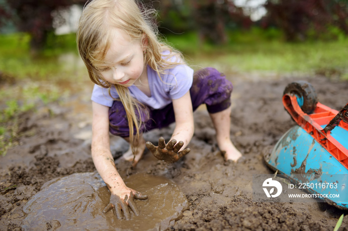 Funny little girl playing in a large wet mud puddle on sunny summer day. Child getting dirty while d