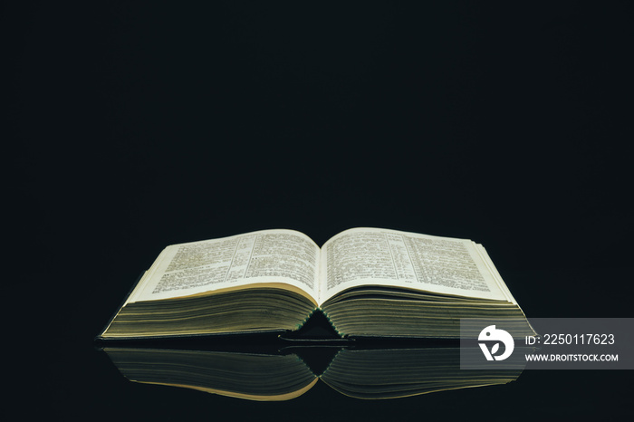 Open Holy Bible on a black glass table dark background