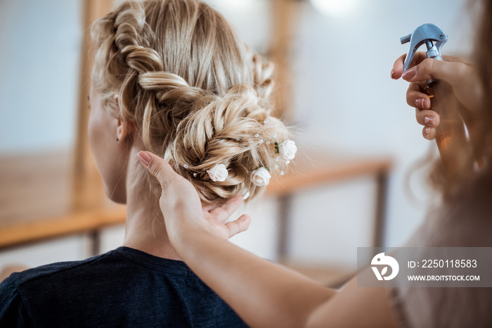 Female hairdresser making hairstyle to blonde girl in beauty salon.