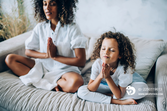 Lovely girl with mother meditating on sofa