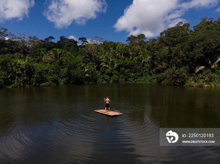 Young man standing on wooden raft float on tropical exotic Amazon rainforest jungle water lake river