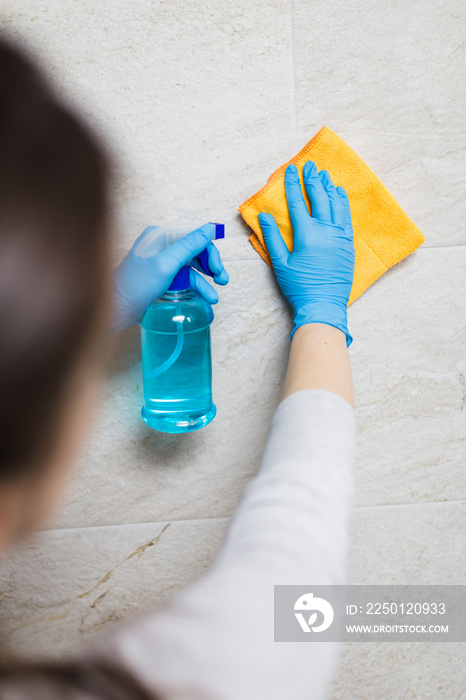 戴着外科防护手套的女佣在浴室里用超细纤维布和消毒剂清洗瓷砖