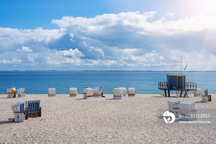 beach chairs and lifeguard tower on wide sand beach against blue sea and sky on sunny day