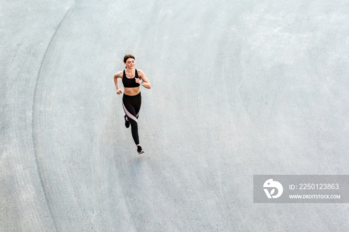 Top view of young attractive athletic woman speed running on city asphalt and workout in the morning