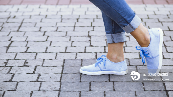 一个穿着牛仔裤和蓝色运动鞋的女孩的腿在人行道的瓷砖上，一个年轻女人穿着夏天的pa漫步
