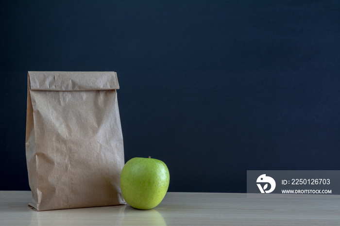 Bolsa de almuerzo de papel en el  pupitre de la escuela con una manzana verde