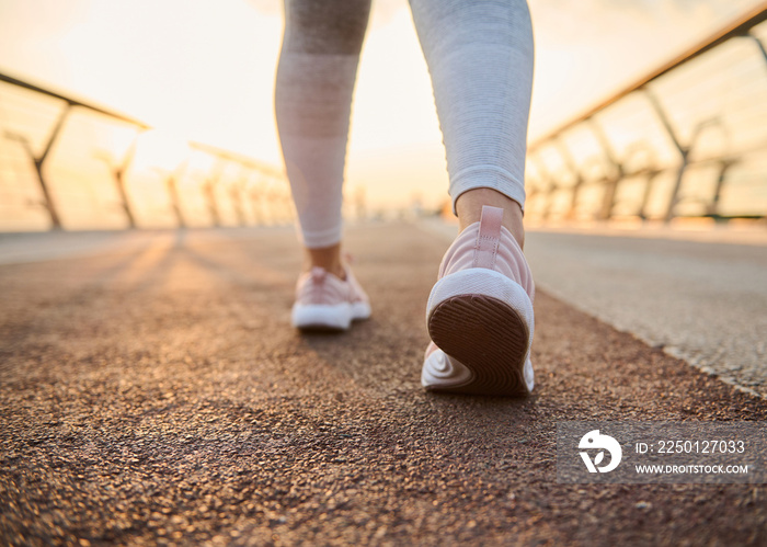 Close-up female athlete feet in pink sneakers on a treadmill at sunrise background. Cropped image of