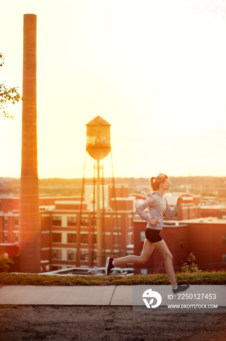 Full length of woman jogging on road by buildings against sky during sunny day