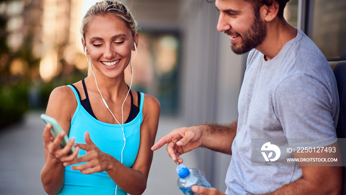 Modern woman and man jogging / exercising in urban surroundings and using cellphone at a pause / bre