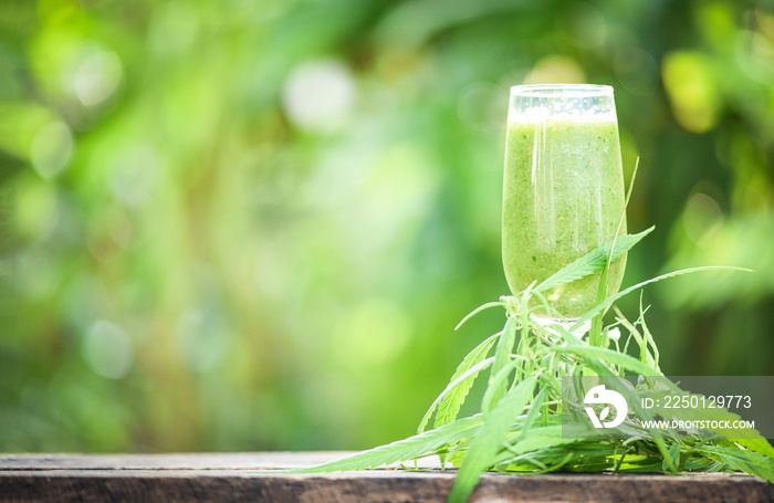 summer juice with green fruit smoothies in glass with cannabis leaf marijuana plant on wooden table 