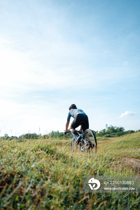 A young bearded cyclist is biking through a field