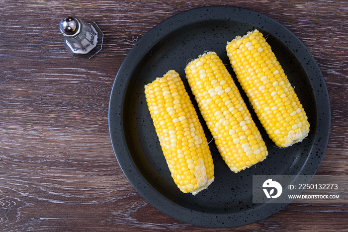 Cooked corn on the cob on a black plate, salt shaker