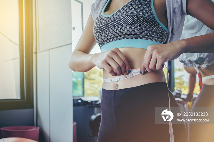 close up of woman checking success of weight loss program with measuring tape at gym.