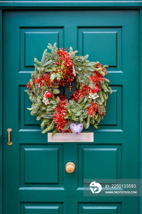 A Christmas crown hanging on a green front door with moldings