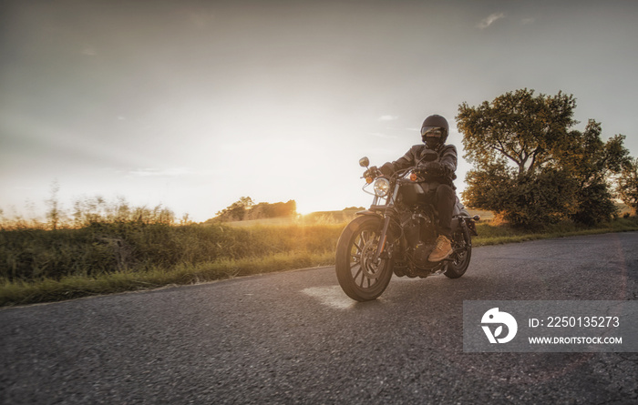 Biker rides his motorcycle along the road during beautiful sunset. Motorbikers season starts now du