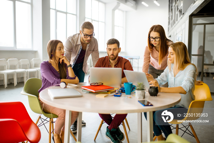 Team of a young coworkers dressed casually working together with laptops sitting at the round table 