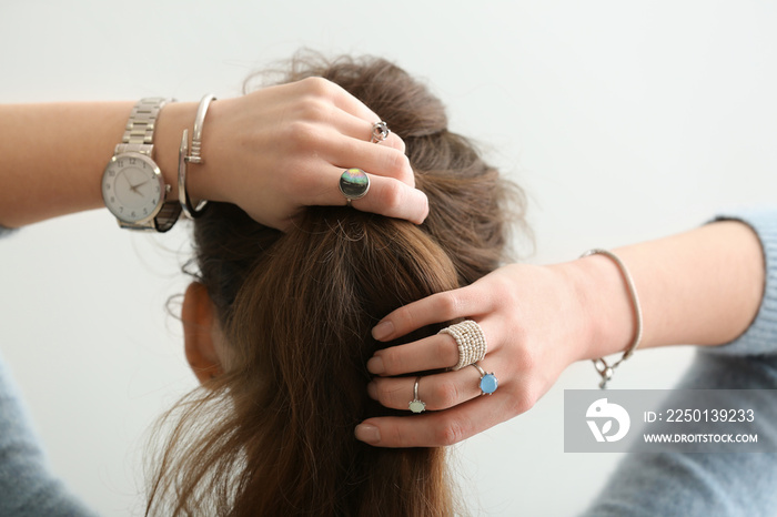 Beautiful young woman with stylish bijouterie doing her hair on white background