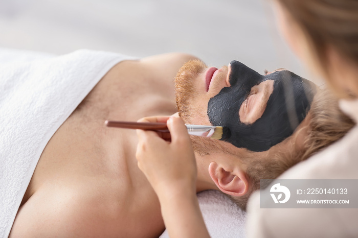 Cosmetologist applying mask on mans face in spa salon