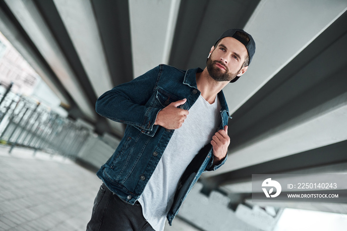 Outdoors leisure. Young stylish man walking on city street wearing wireless earphones listening to m