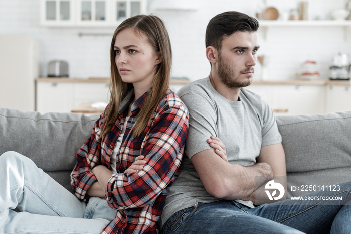 Young couple experiencing problems in relations sitting next to each other but unwilling to communic