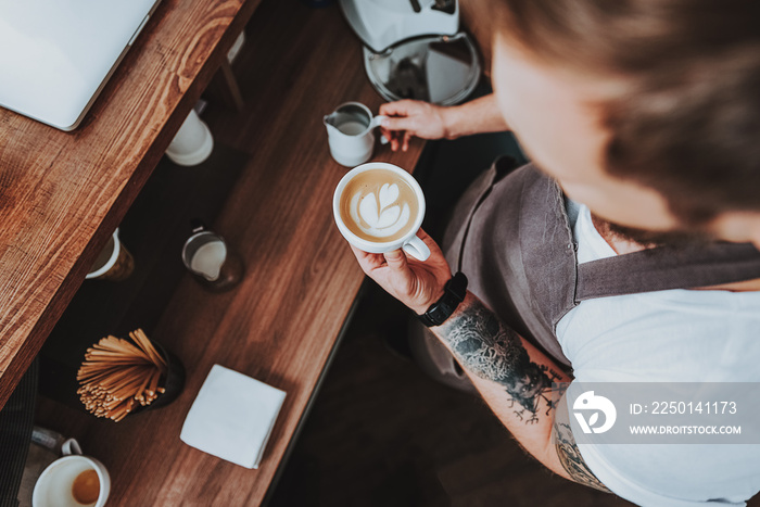 Top view of tattooed barista holding cup with latte