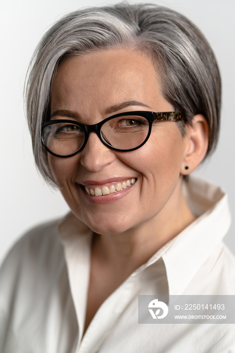 Pretty gray haired woman smiling at camera. Mature woman in eyeglasses and white shirt broadly smile