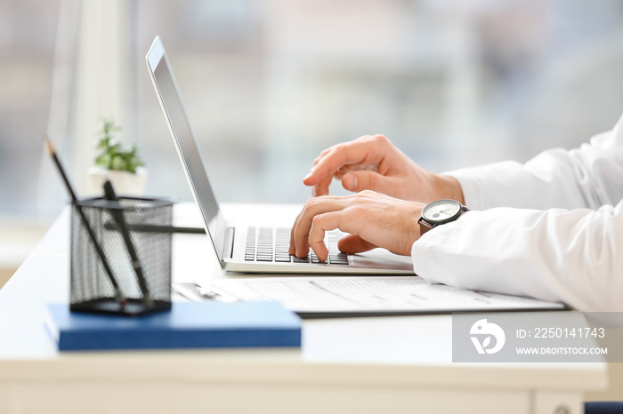 Young doctor using laptop in clinic, closeup