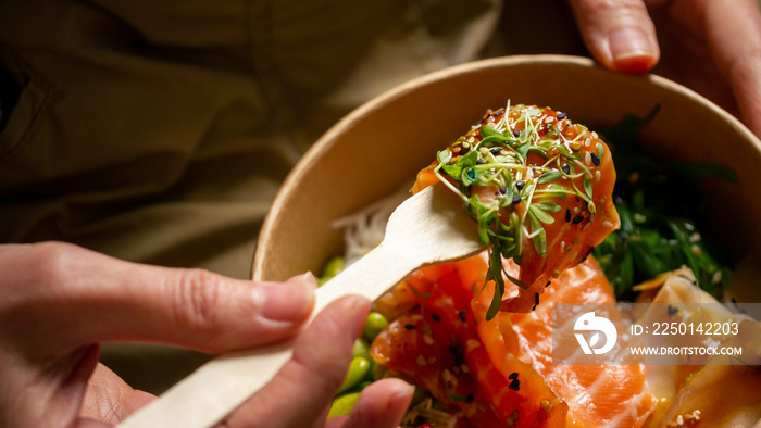 Female enjoying quick gourmet lunch - plastic-free, recyclable take away bowl with raw fish, rice an