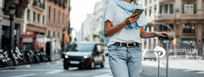 Young traveling woman with suitcase on a sunny city street. Traveler on vacation. Waiting for taxi