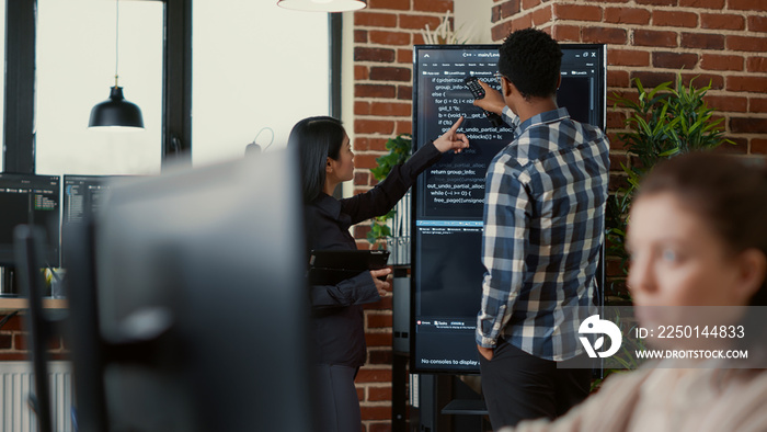 System developers analyzing code on wall screen tv looking for errors comparing results on digital t