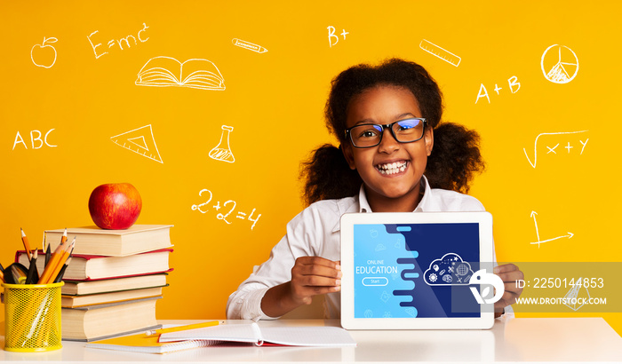 教育理念。女孩展示平板电脑，坐在黄色背景的桌子旁，围绕着公式和sc