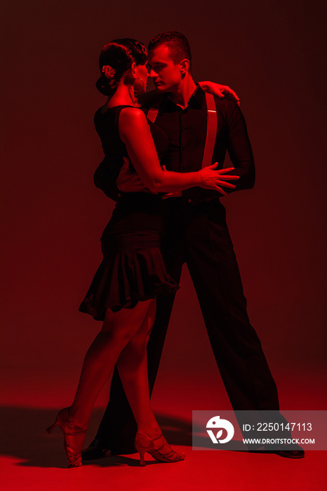 sensual couple of dancers performing tango on dark background with red illumination