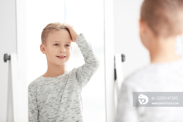 Cute little boy looking at himself in mirror indoors