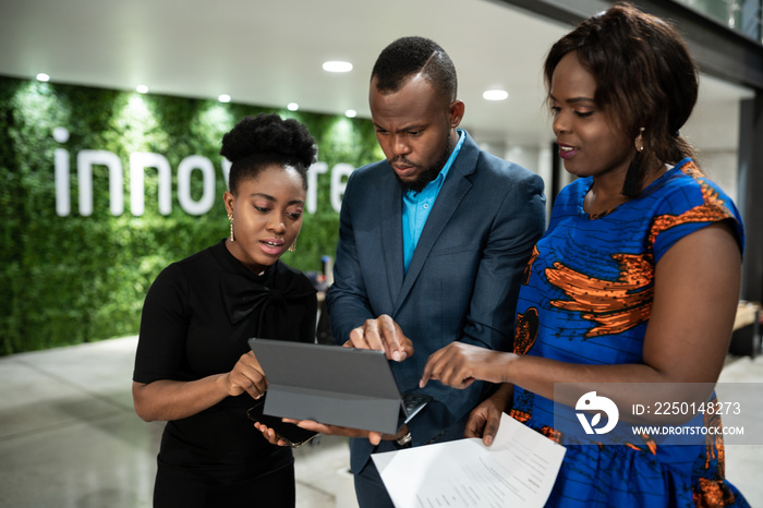 African businesspeople using a tablet together in an office lobby