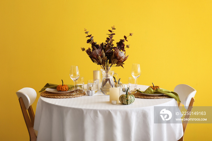 Beautiful table setting with fresh pumpkins and candles near yellow wall