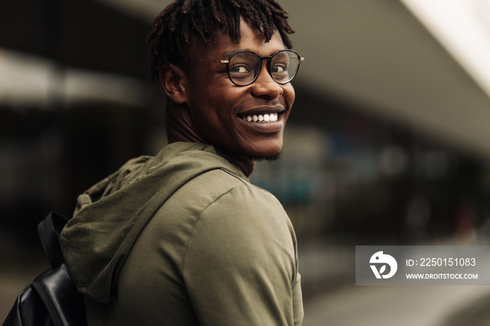 Happy successful african student, wearing glasses and with a black backpack, standing on the steps a