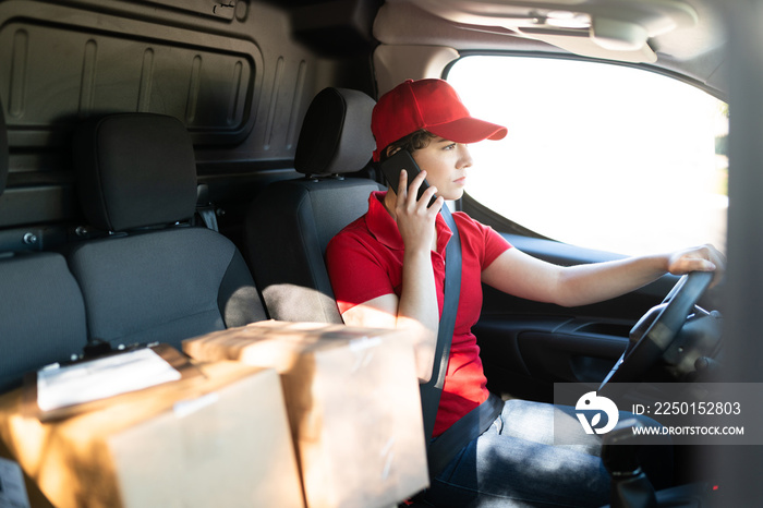 Young courier talking on the phone while driving a delivery truck