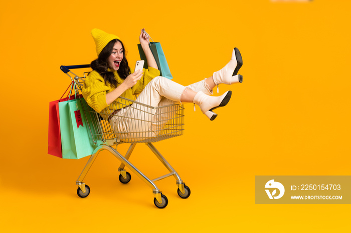 White excited woman laughing and using cellphone in shopping cart