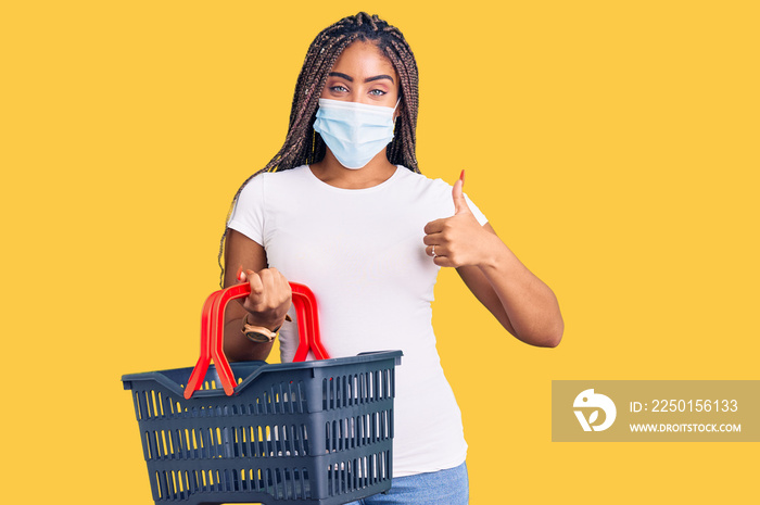 Young african american woman with braids wearing shopping basket and medical mask smiling happy and 