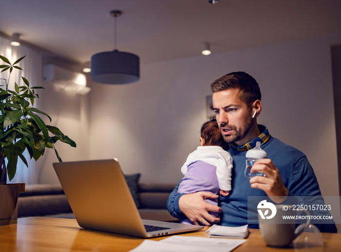 A busy super-dad feeding his baby girl and having online meeting at home.