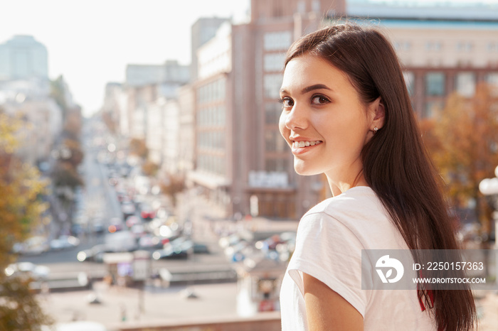 Gorgeous woman smiling to the camera over her shoulder, busy city streets on the background