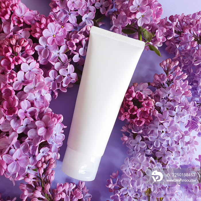 White Cream tube and pink violet lilac flowers on purple background. Cosmetic skincare product blank