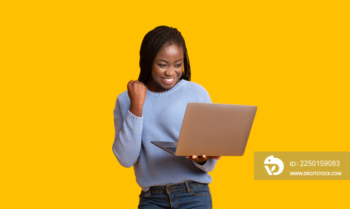 成功的黑人女孩拿着笔记本电脑庆祝战胜黄色背景