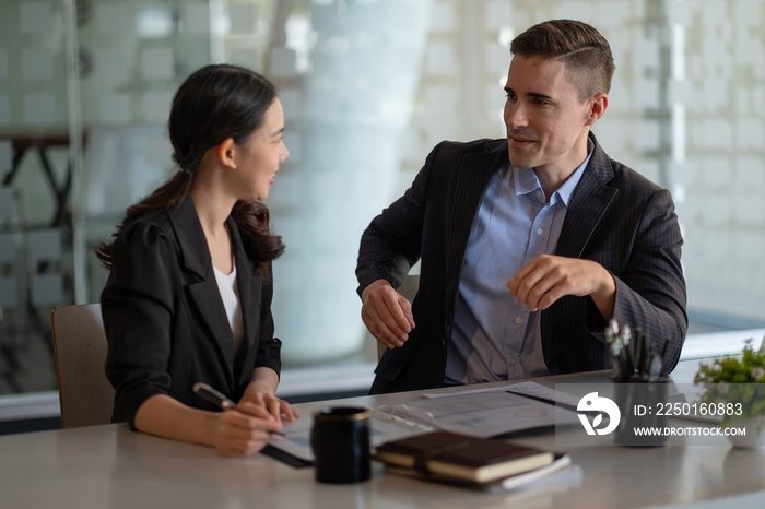 Multiethnic male caucasian mentor and female asian sitting at desk with laptop doing paperwork toget