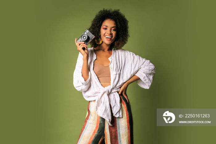 Afican woman holding retro photocamera and  laughing over green background in studio.