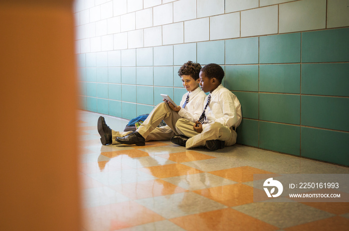 Portrait of two schoolboys (8-9, 10-11) sitting on floor in school corridor using digital tablet